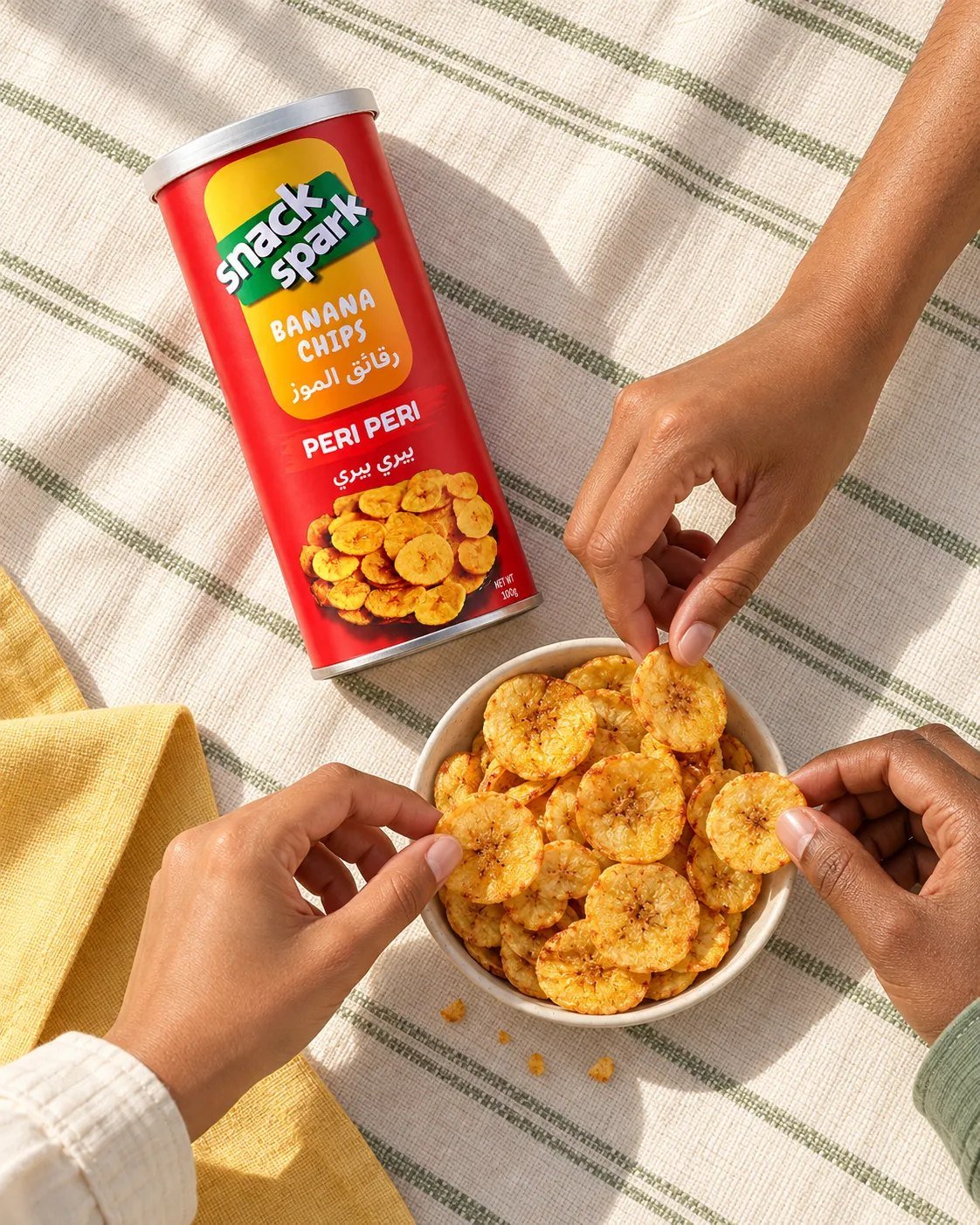 Friends reaching into a bowl of Peri Peri banana chips on a picnic blanket